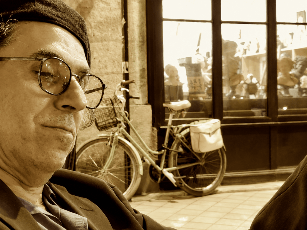 François W. Beydoun en réflexion, attablé devant la vitrine d'un atelier, un vélo vert en arrière-plan